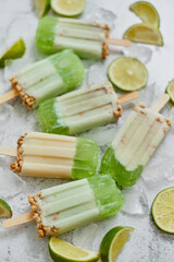 Lime and cream homemade popsicles or ice creams placed with ice cubes on gray stone backdrop