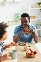 African happy father having breakfast together with his son they sitting at the table and talking in the kitchen
