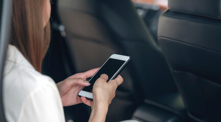 Young businesswoman using smartphone while sitting on the passenger seats in the car.