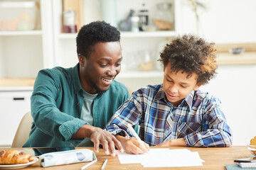 African smiling father helping to his son doing his homework they sitting at the table in the room