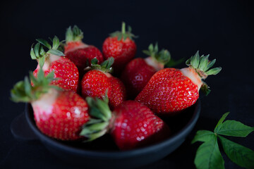 Fresh juicy strawberries in a black plate on a black matte background