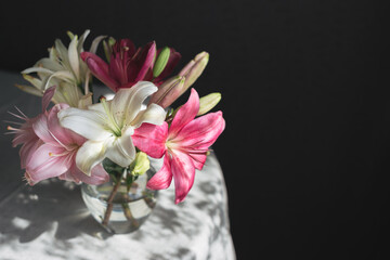 Romantic bouquet of the white and pink lilies in a glass vase on a dark background  in sunlight.