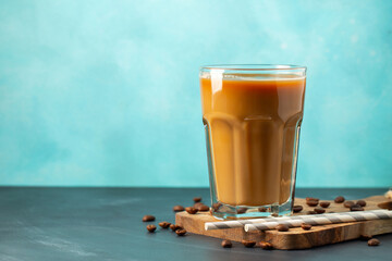 Ice coffee in a tall glass with cream poured over and coffee beans on a light stone background....