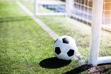 Soccer ball with sunlight and shadow on green field in front of goal post. The Football in front of goal line. It is not yet goal.