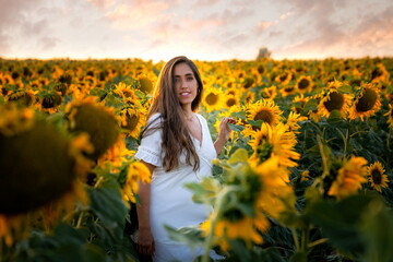 Woman among sunflowers in white dress and smiling at sunset