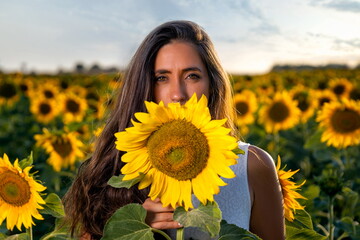 Woman among sunflowers in white dress with face behind sunflower