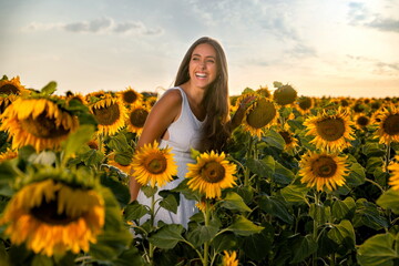 Woman among sunflowers in white dress and smiling at sunset