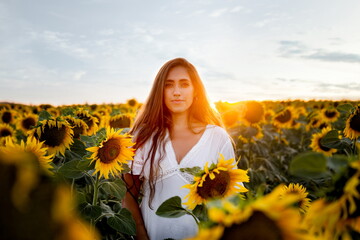 Woman among sunflowers in white dress at sunset