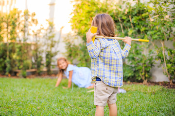 Kids playing croquet on grass yellow stick and ball