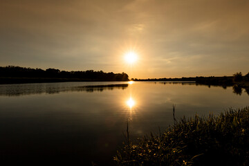 Obraz premium Scenic view of Sunset above the lake. Evening with cloudy sky background and reed grass at foreground. Landscape photo