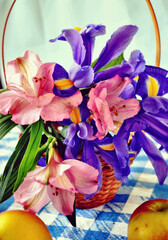 Fototapeta na wymiar Basket with spring iris flowers and Peruvian lilies, apples on the blue-white checked tablecloth, vertical view, spring background 