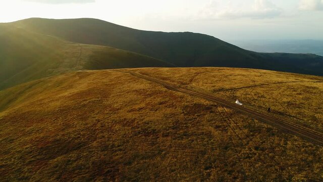 Wedding walk. The groom follows his wife on the mountain top of Mount Gemba. Ukrainian Carpathian Mountains. Aerial view.
