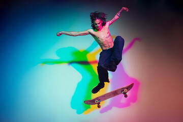 Fototapeta na wymiar Skateboarder doing a trick isolated on studio background in colorful neon light. Young man shirtless riding and skateboarding in motion. Concept of leisure activity, sport, extreme, hobby and motion.