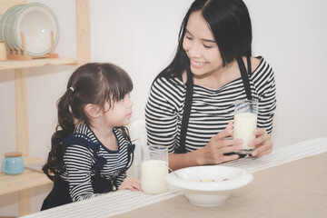 Obraz na płótnie Canvas Happy family of asian mom is drinking milk with her cute daughter in the morning. Photo series of family, kids and happy people concept.