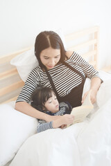 Happy loving family young asian mother reading a bed time story book to her daughter in ...