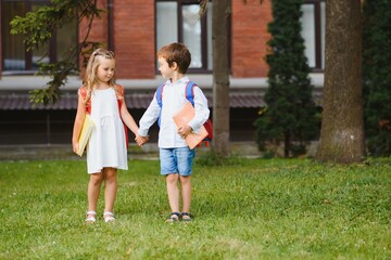 Happy children - boy and girl with books and backpacks on the first school day. Excited to be back to school after vacation. Full length outdoor portrait.