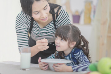 Happy family of asian mother feeding healthy breakfast to her cute daughter in the morning. Photo series of family, kids and happy people concept.