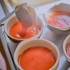 Serving hot steamy tomato soup into rustic dishes using a ladle