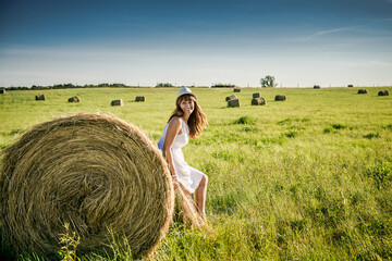 Naklejka na ściany i meble girl and hay. Rural life. Holidays in the village. Beautiful girl is resting after work. girl on the field with hay. Woman near a sheaf of hay in a field.