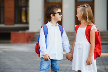 Happy children go back to school. Pupil of primary school go study with backpack outdoors. Kids go hand in hand. Beginning of lessons. First day of fall. Boy and girl from elementary student.