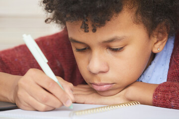 Close-up of serious African boy concentrating on study he sitting at desk and doing paperwork