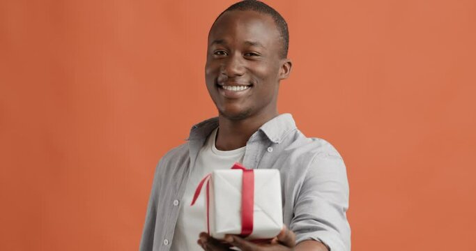 Happy black man giving gift, greeting with holiday to camera