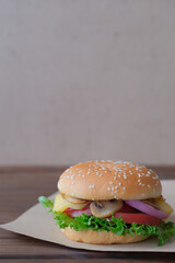 Burger with mushrooms, tomatos, lettuce, onion and cheese on dark wooden background. Vertical view. Copy space.