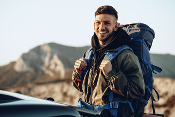 Portrait of a young traveler man in hiking equipment standing near his off-road car