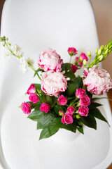 A beautiful bouquet of tender pink peonies and small roses stands on a white chair. Suitable for bridal bouquet, birthday. Close-up, top view.