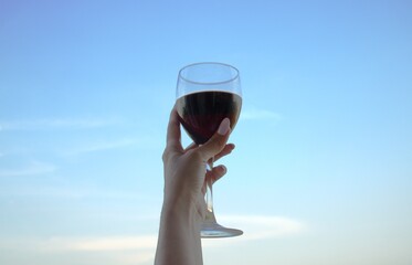 рука держит бокал вина на голубом небе