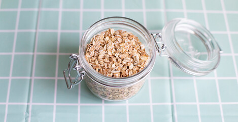 Healthy breakfast Organic oat flakes in a glass jar on a turquoise background. Oatmeal. Selective focus. Top view. Selective focus, copy space. The concept of vegetarian and organic food.
