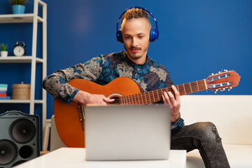 Young man sitting in his room and watching guitar tutorial on laptop