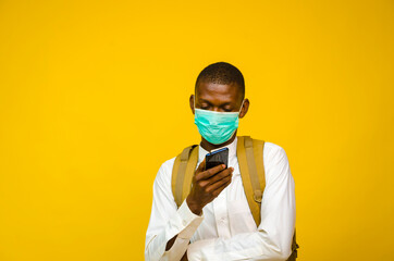 a young handsome african man wearing face mask isolated over yellow background as he prevent himself from the out break in the society and operating his cellphone