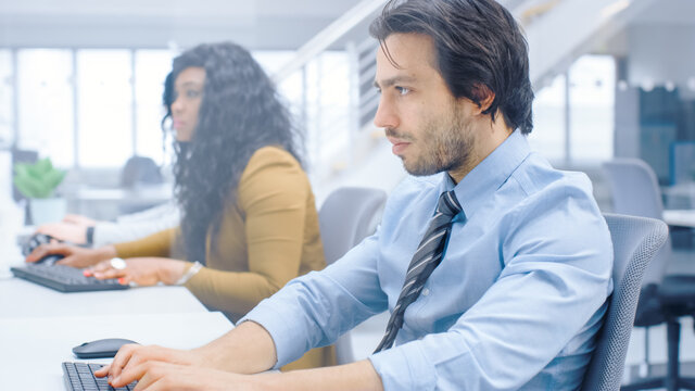 Handsome Businessman, Economist, Stock Broker Uses Desktop Computer, Typing on a Keyboard, Looking At Graphs and Statistics. Confident Young Businessman Works in the Big Corporate Firm Office