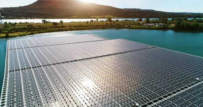 Floating solar panels in a blue pond under the sunlight. We can see the panels floating on water with mountains in the background - aerial view 4K