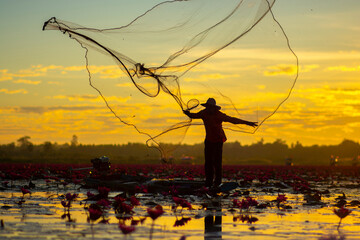 A fisherman casting a net into the water during on sunsrise. Silhouette.
