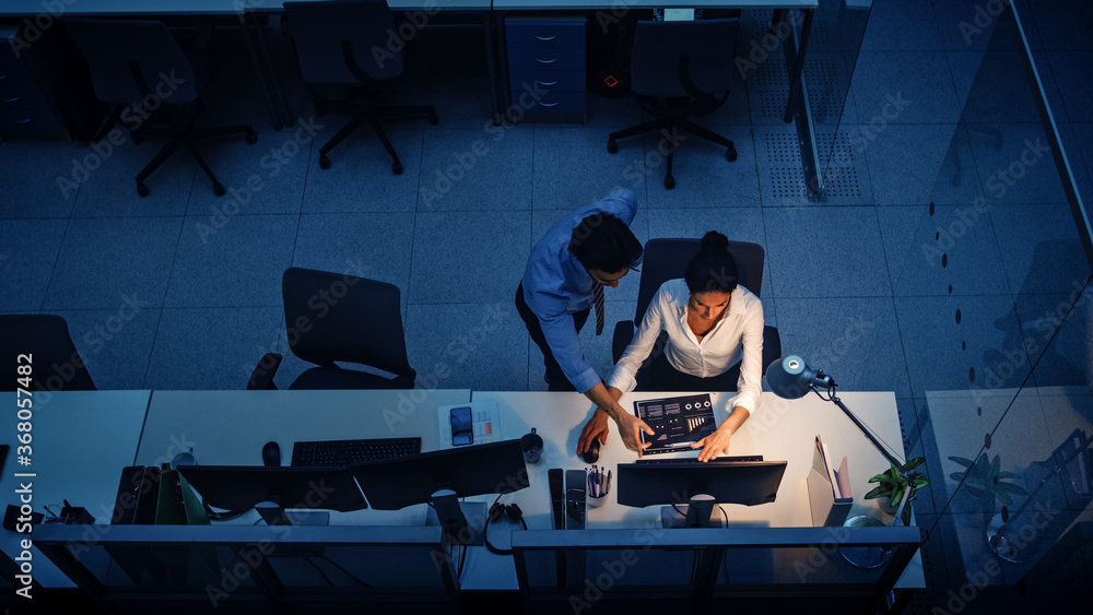 Aufkleber working late at night in the office: businesswoman and businessman using desktop computer, having di