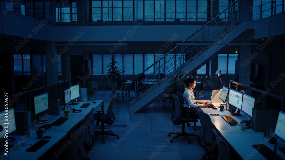 Poster alone working late at night in the office: businesswoman using desktop computer, analyzing, using do