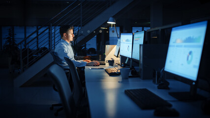 Working Late at Night in the Office: Businessman Uses Desktop Computer, Analyzing, Using Documents, Solving Problems, Finishing Important Project. Diligent Ambitious Young Worker