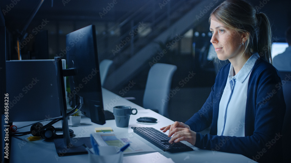 Poster working late at night in the office: businesswoman using desktop computer, analyzing, using document