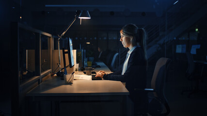 Working Late at Night in the Office: Businesswoman Using Desktop Computer, Analyzing, Using Documents, Solving Problems, Finishing Project. 
