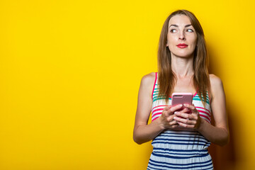 Serious young girl with a phone looks to the side on a yellow background