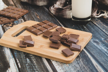 milk dark chocolate tiles on wood cutting board, wooden background