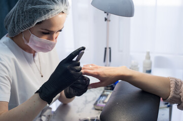 Manicure master in a mask and gloves in the salon. Care at a social distance. Security