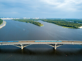 The trains of the Kiev metro are going on the bridge over the Dnieper river. Clear sunny summer day. Aerial drone view.