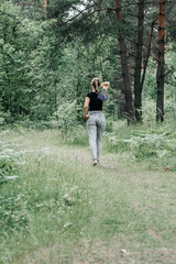 young woman with a tail of hair in a black t-shirt and gray jeans in the woods holding blue wildflowers in her hands