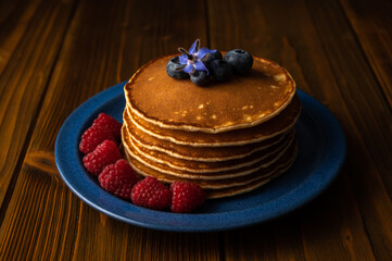 Fresh pancakes with berries on the wooden table. Closeup view. Low Key Food Photography