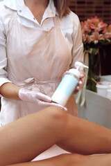  a female cosmetologist in a pink apron and gloves and a white coat smears cream from a tube on the feet of a patient in the office      