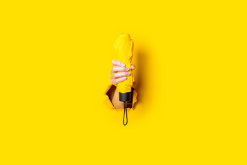 Female hand holds a yellow umbrella on a yellow background