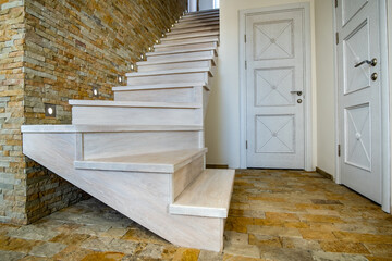 Stylish wooden contemporary staircase inside loft house interior. Modern hallway with decorative limestone brick walls and white oak stairs.